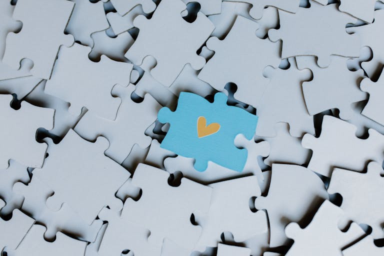 Juntosseguros A standout blue puzzle piece with a heart symbol among white puzzle pieces, showing uniqueness.