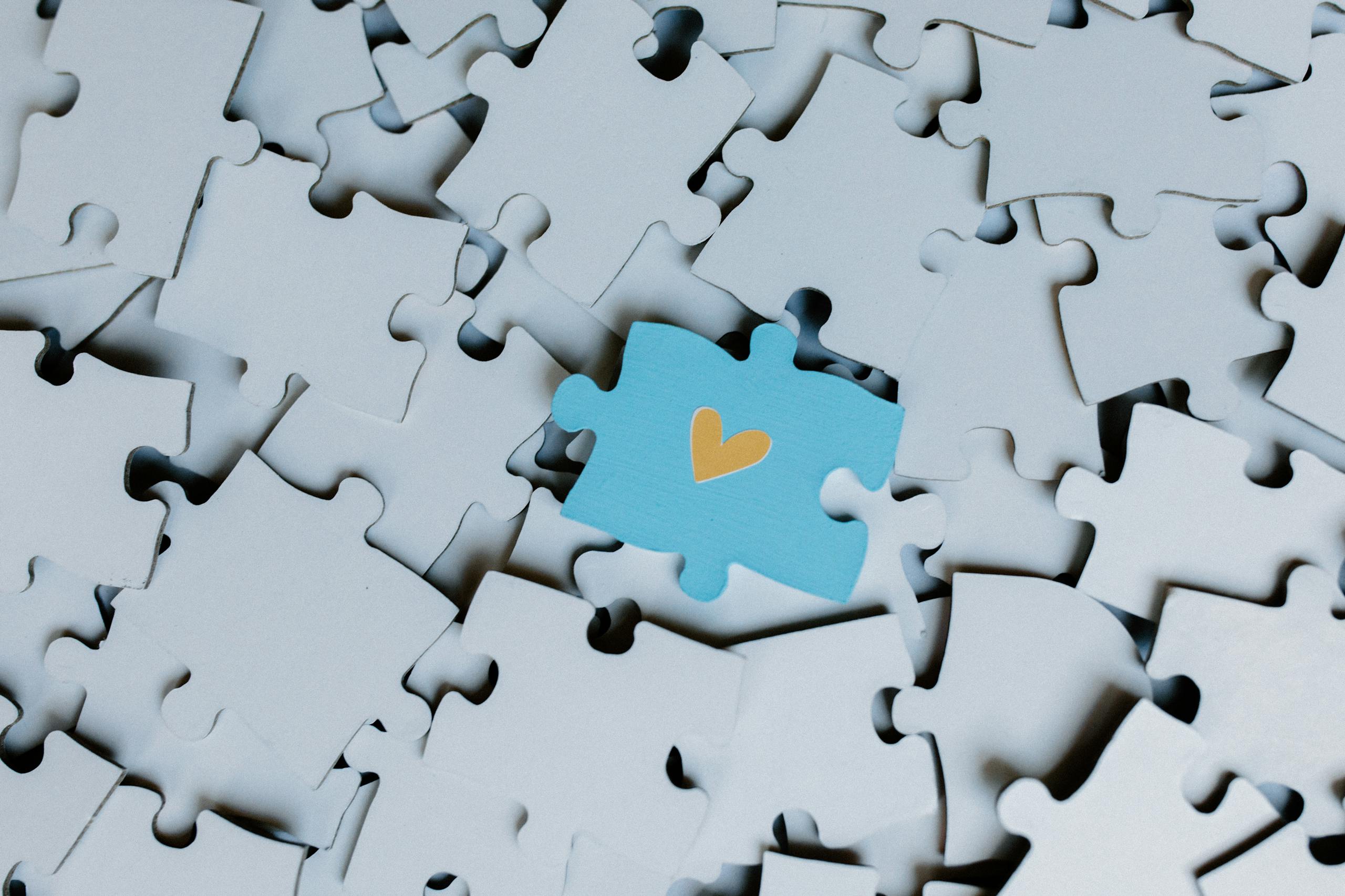Juntosseguros A standout blue puzzle piece with a heart symbol among white puzzle pieces, showing uniqueness.