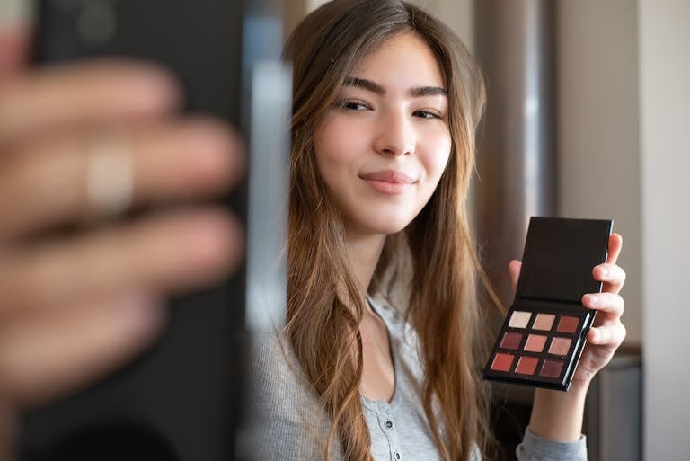 Lufanest A young woman live streaming a makeup tutorial from her home office, using a smartphone.