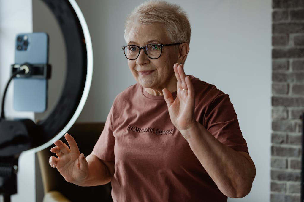 Dolfier Elderly woman making online video content at home with ring light and phone.