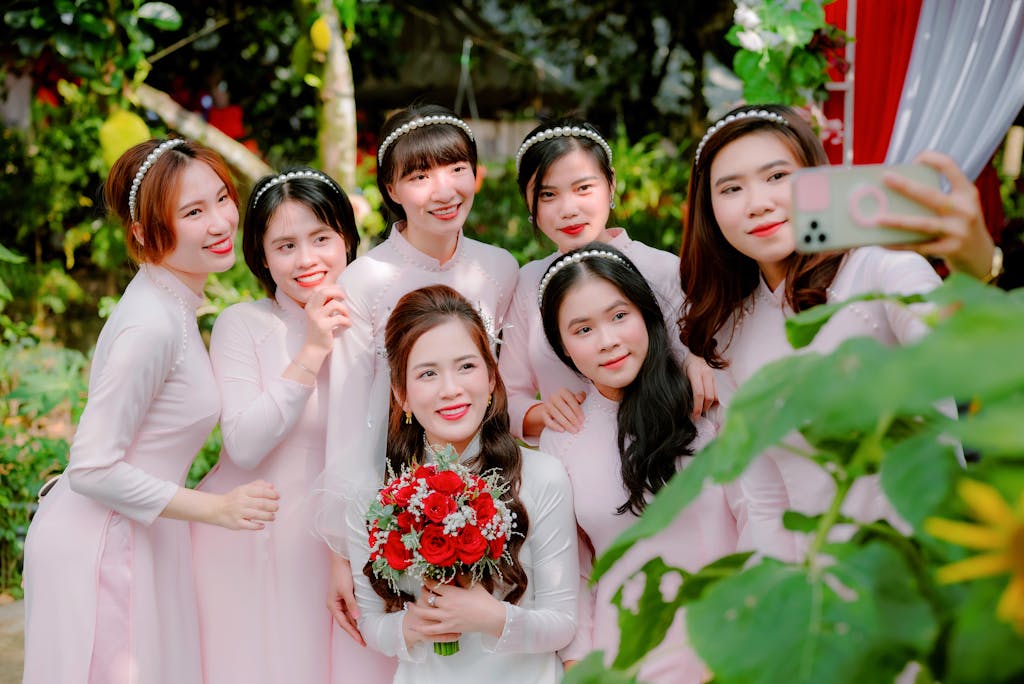 SocialMediaGirls Forum Group of smiling bridesmaids in traditional dresses posing for a selfie at an outdoor wedding.