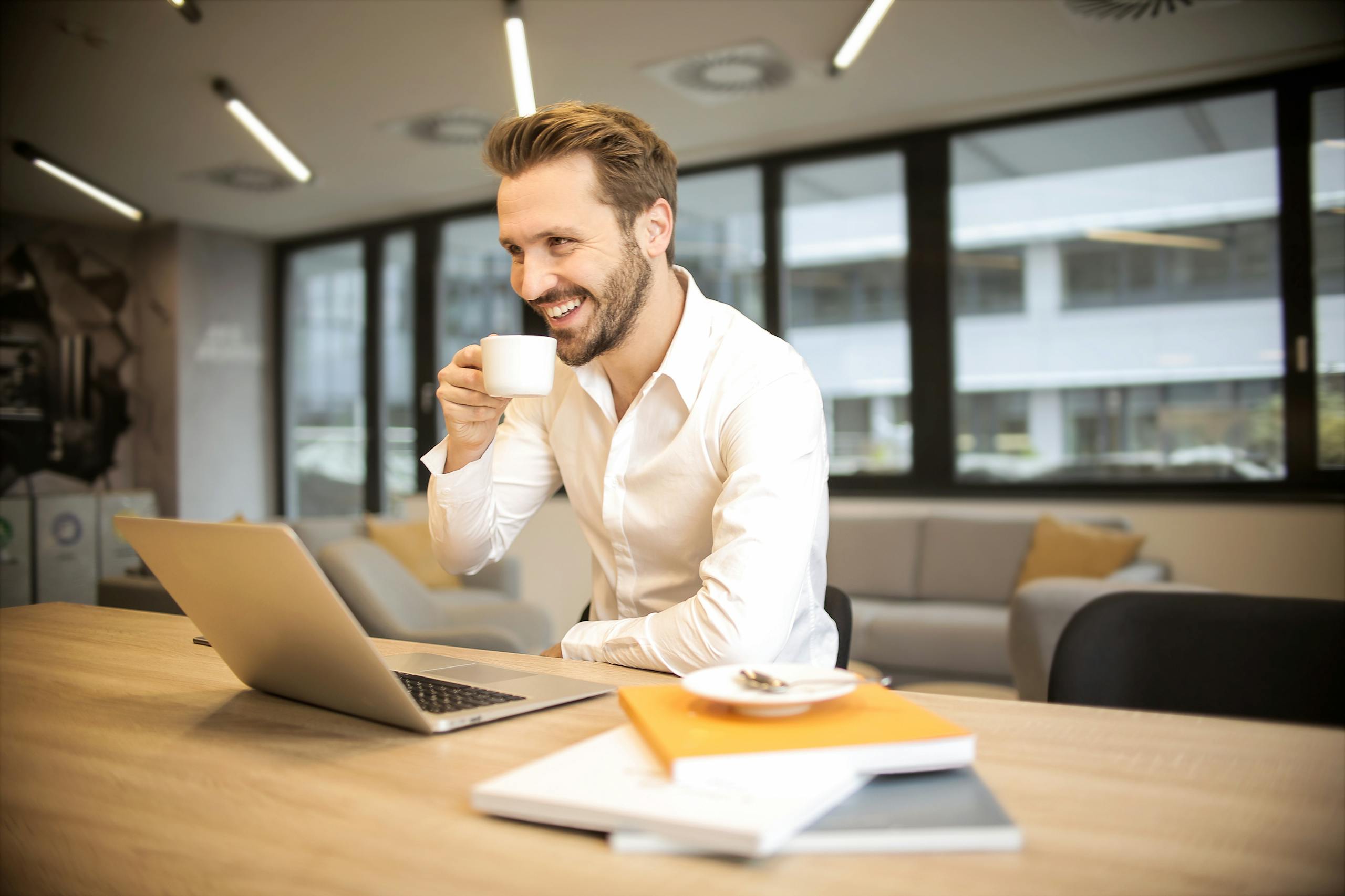 Entrepreneur Break Man enjoying a coffee break while working in a modern office with laptop and books.
