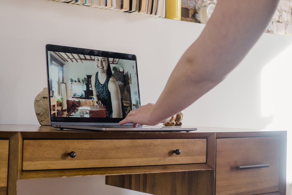 Dolfier Person gesturing towards a laptop displaying a video call participant in a cozy room.