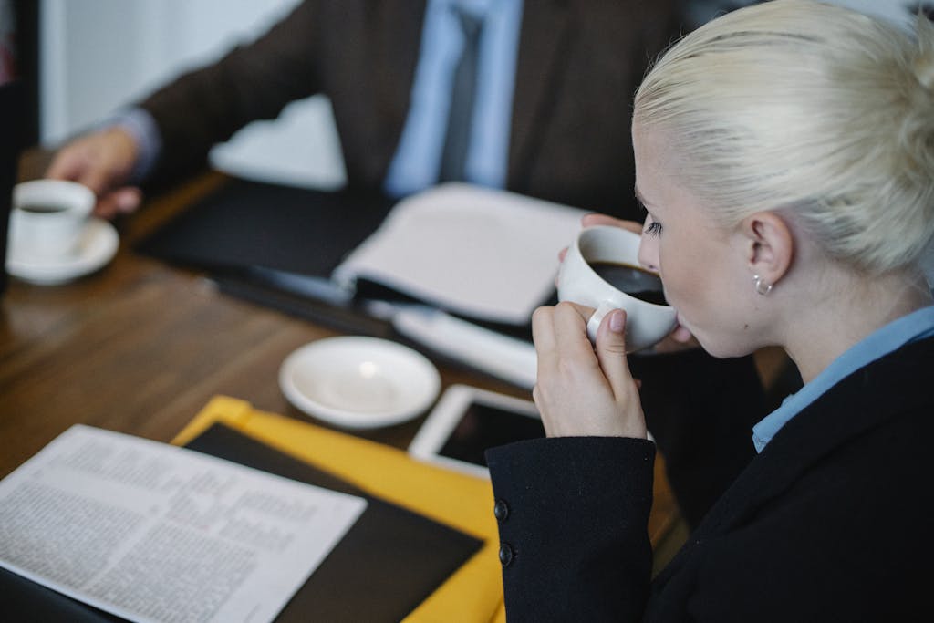 Entrepreneur Break Side view of female in formal clothes drinking hot coffee while sitting at table with documents during business meeting