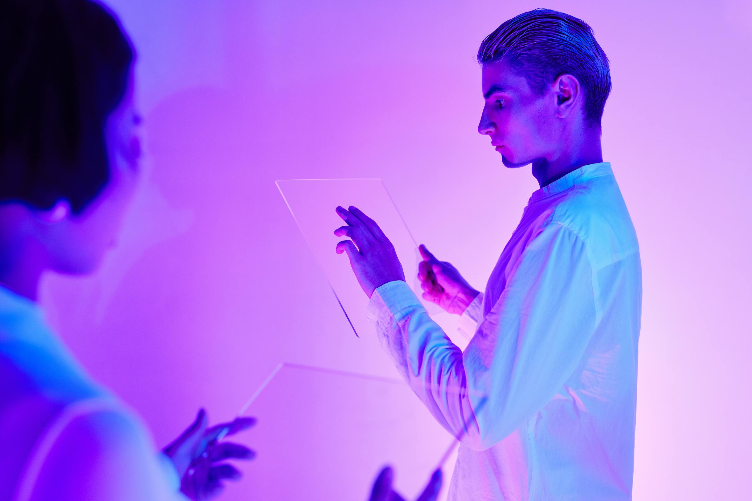 Edivawe Two individuals engaging with futuristic transparent touch screens in a vibrant purple-lit studio.