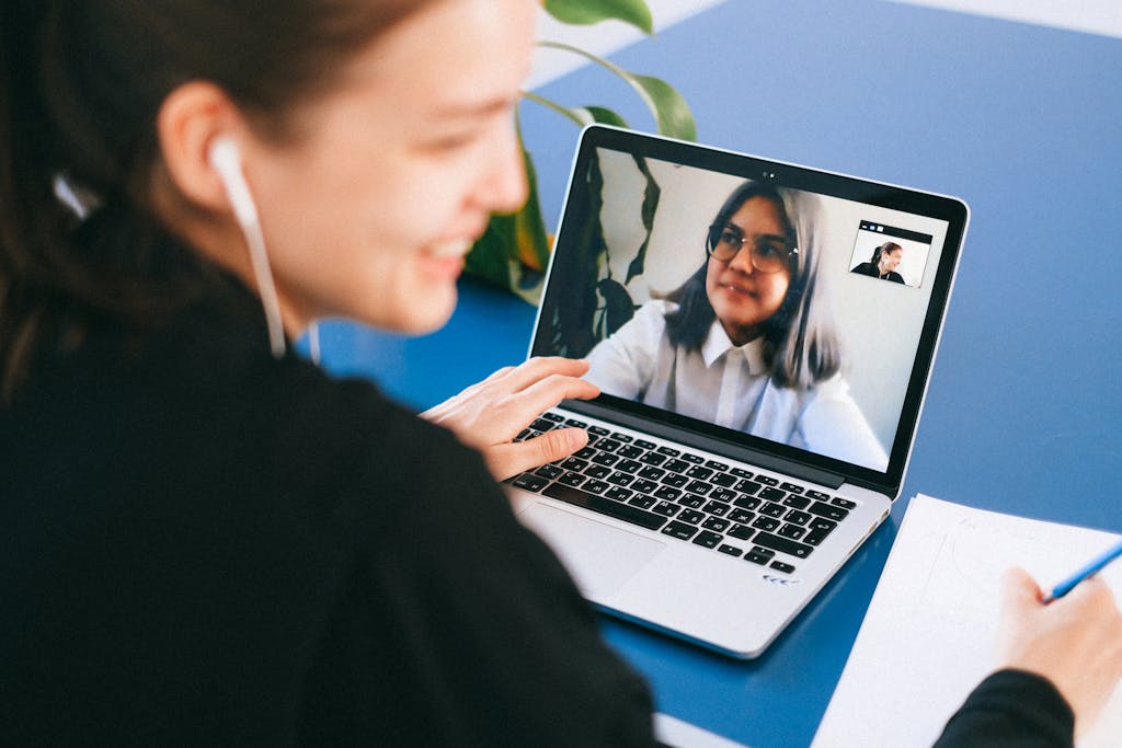 Hormita Woman having a video conference on a laptop, smiling and taking notes.