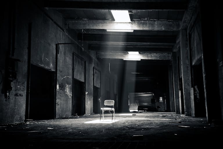 Carmela Clouth A haunting black and white photo of an abandoned warehouse with a solitary chair illuminated by sunlight through a window.