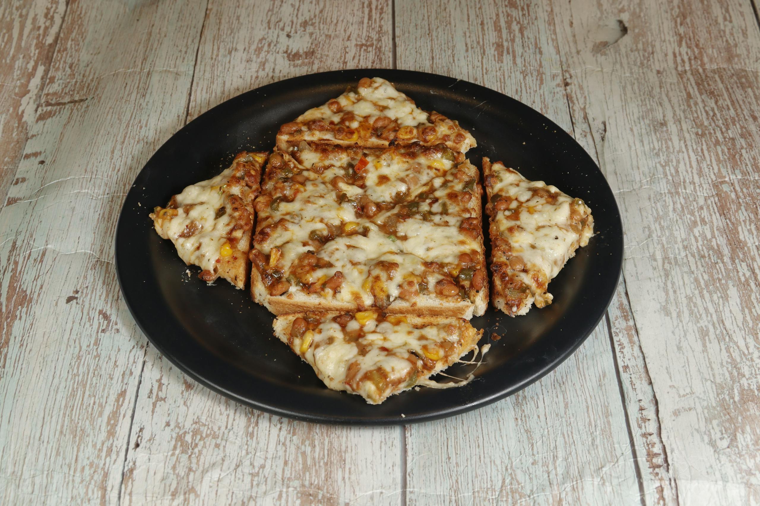 ChatPic A close-up view of cheesy pizza slices on a black plate, set on a rustic wooden table, perfect for food blogs.