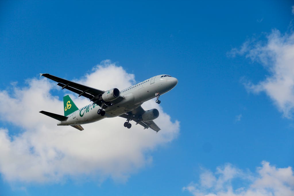 openskynews A commercial airplane with green tail in flight against a bright blue sky with clouds.