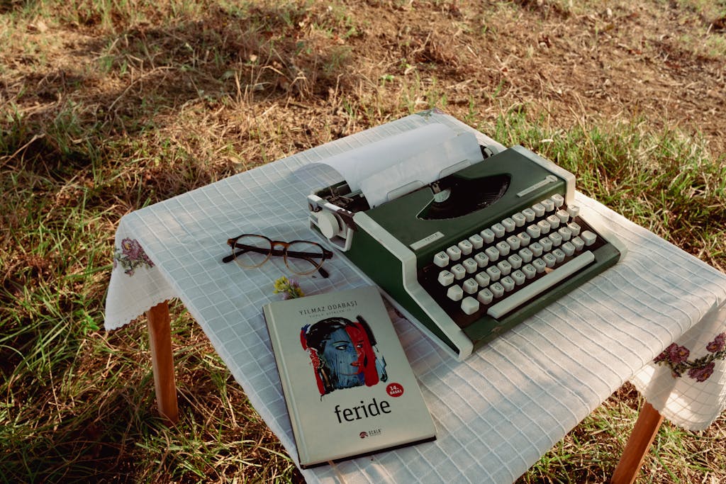 Serlig A green typewriter and book on a tablecloth-covered outdoor table.