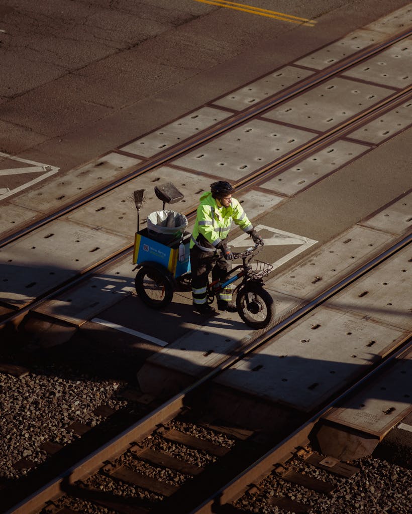 Matarecycler A street cleaner on a bicycle pauses while crossing railway tracks in an industrial setting.