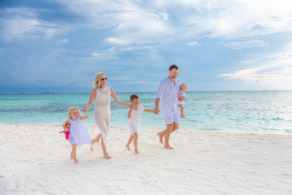 FamousParentingMomlife Family enjoying a walk on a pristine beach with turquoise waters, captured in a light-hearted moment.