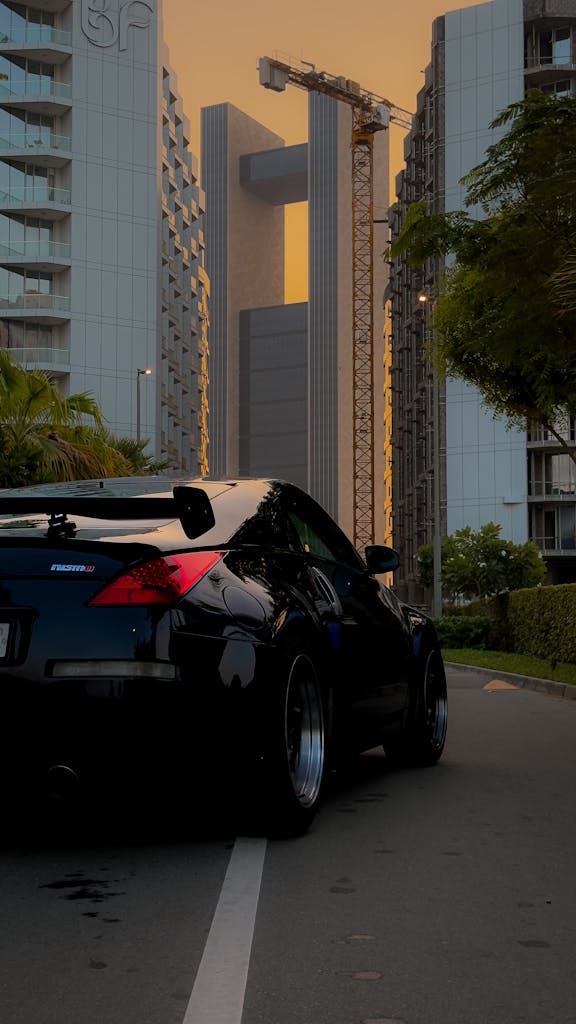 Monthly Car Rental Bahrain Stylish black sports car on an urban street in Bahrain, framed by towering skyscrapers at sunset.