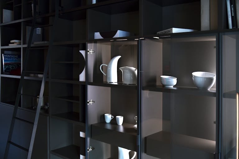 Memorandum to Cabinet Stylish display of white ceramic tableware on dark shelving in contemporary setting.