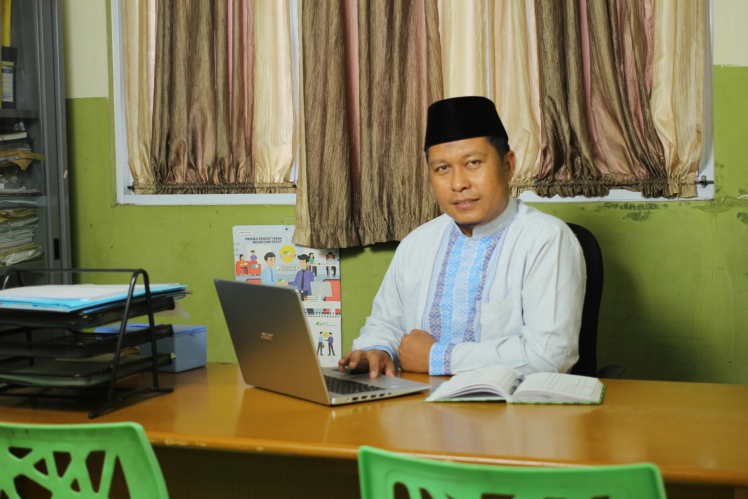Dojen Moe Successful Indonesian teacher working at a desk in a traditional outfit.