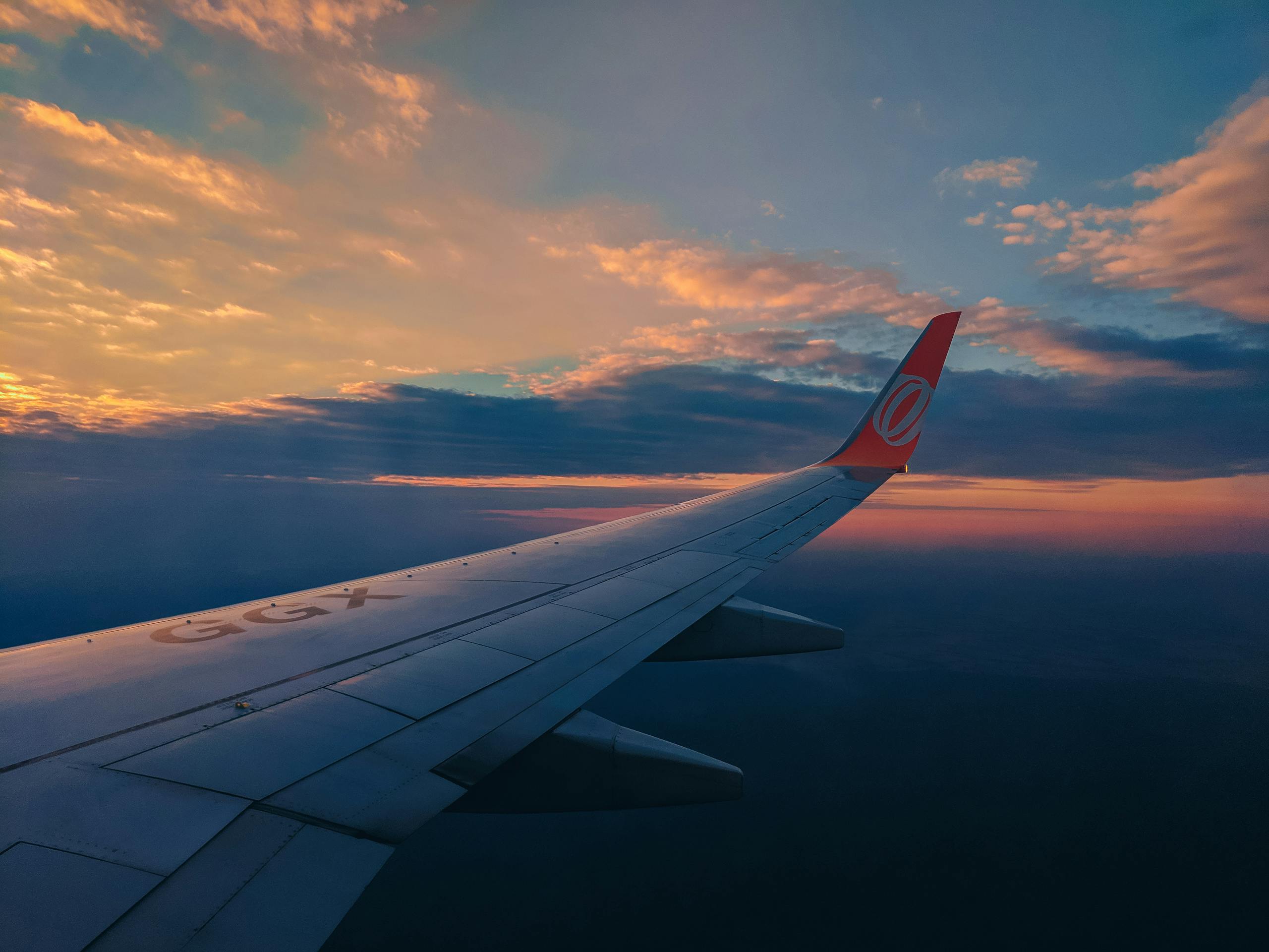 openskynews View of an airplane wing soaring above a vibrant sunrise cloudscape, emphasizing travel and adventure.